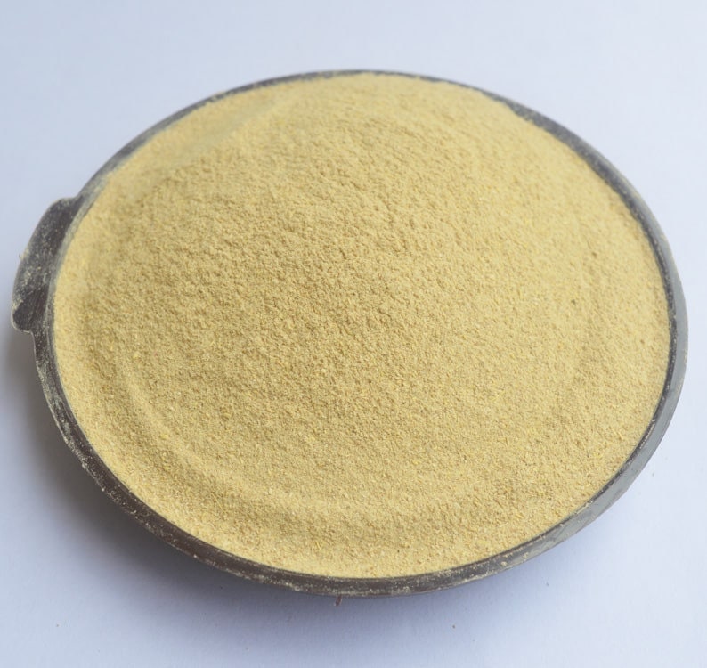May include: A close-up of a light yellow powder in a black bowl. The powder is finely ground and has a smooth texture.