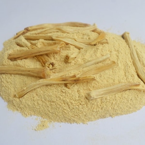 May include: A pile of light yellow powder with several long, thin, light brown sticks on top.