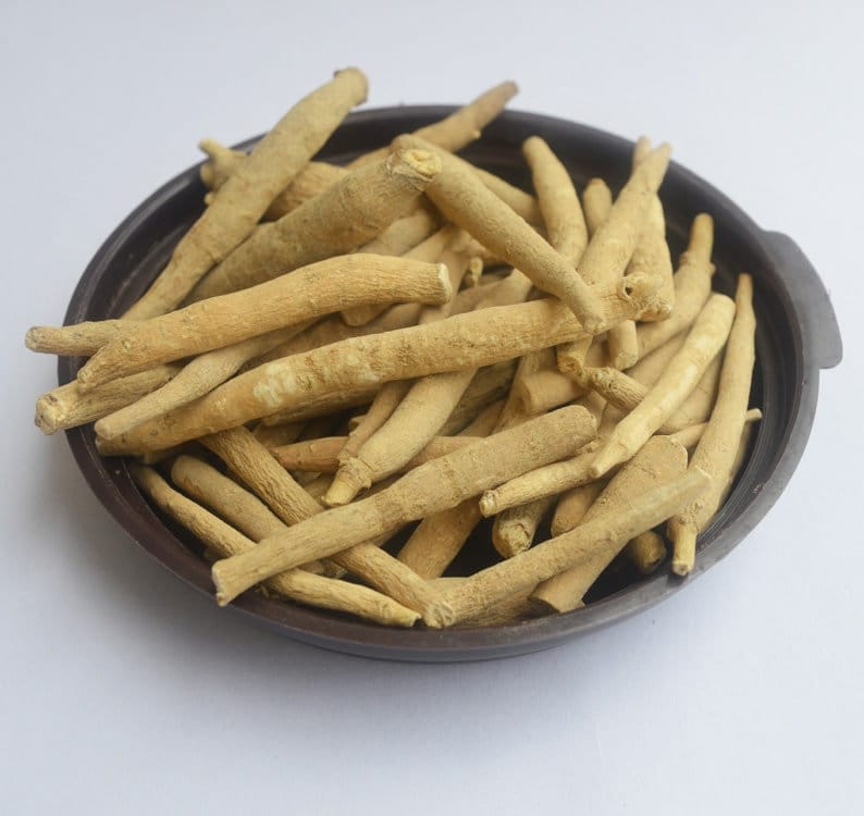 May include: A close-up of a bowl filled with dried, light brown, thin, and long herbal roots. The roots are arranged in a random pattern and are piled high in the bowl.