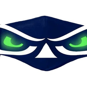 May include: Navy blue face mask featuring a stylized eye design with glowing green eyes and white accents. The mask has adjustable black ear loops. The design is centered on the mask.