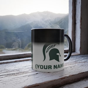 May include: Black and white color changing mug with a green Spartan helmet logo and the text "(YOUR NAME)" on the front.