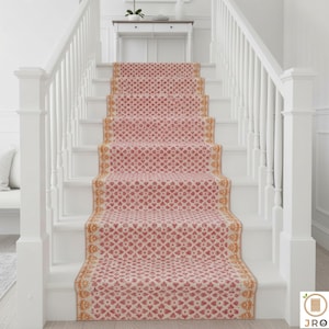 May include: A stair runner featuring a repeating heart pattern in red and cream. The runner is edged with a gold and cream design. The stairs are white with white banisters. The runner adds a decorative touch to the staircase.