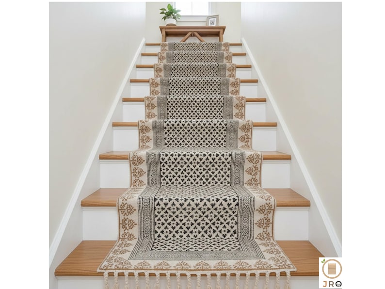 May include: A stair runner with a geometric pattern in black and beige. The runner is installed on wooden stairs with white risers. The runner has a fringe at the bottom and a decorative border.