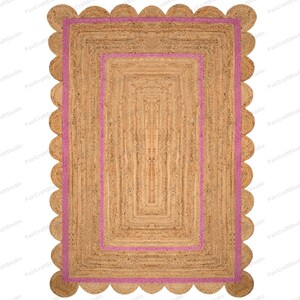 May include: A rectangular jute rug with a pink border and scalloped edges. The rug has a woven texture and a natural brown color.