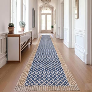 May include: A long, rectangular blue and white patterned rug with a geometric design, featuring a beige border and fringe. The rug is placed in a hallway with hardwood flooring and a white cabinet.