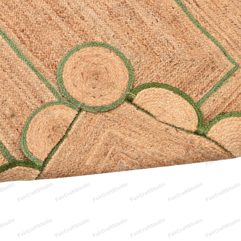 May include: A natural fiber rug with a geometric pattern. The rug is made of jute and has a green border. The rug is woven with a textured pattern.