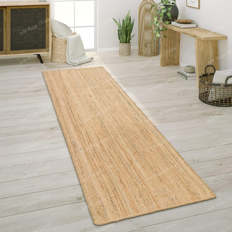 May include: A natural fiber runner rug made from jute. The rug has a light brown color and a woven texture. It is placed on a light wood floor.