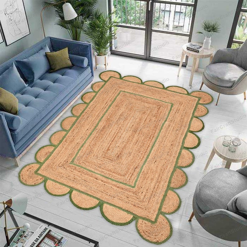 May include: A large, rectangular jute rug with a green border and scalloped edges. The rug is laid out on a light-colored floor in a living room setting.