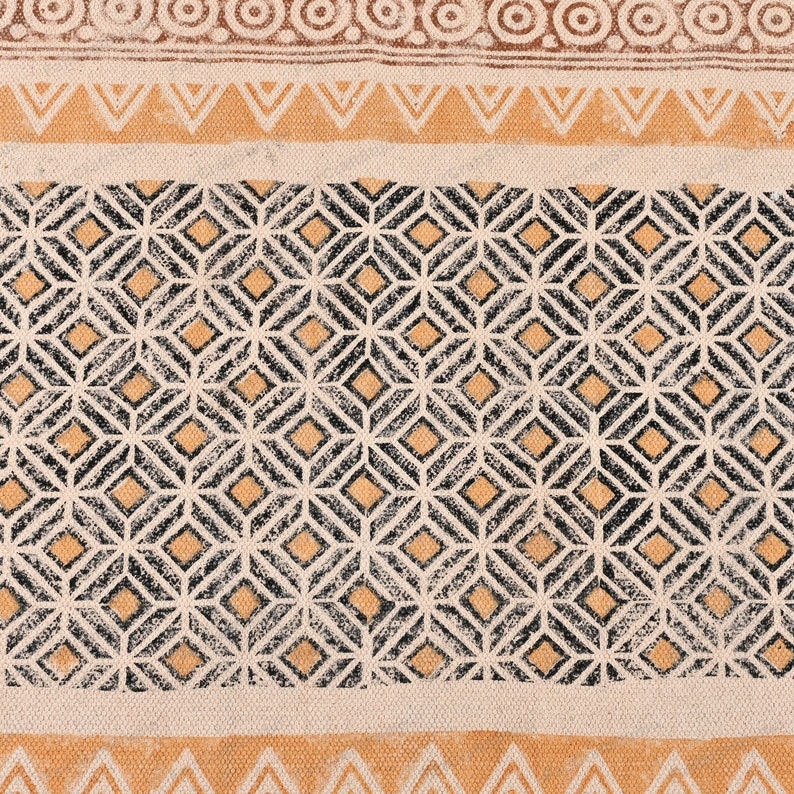 May include: A beige fabric with a black and orange geometric pattern. The pattern is made up of repeating diamonds and squares.