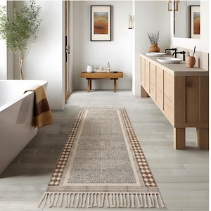 Puede incluir: Una alfombra rectangular para baño con un diseño geométrico y flecos. La alfombra presenta un diseño central de pequeños cuadrados y un borde de diamantes alternos en tonos beige y marrón. La alfombra mide aproximadamente 152 cm de largo.