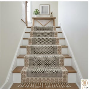 May include: Stair runner rug with a geometric pattern in beige, brown, and cream. The runner features a repeating diamond and floral design, with a fringe at the bottom. The stairs have white risers and wooden treads.