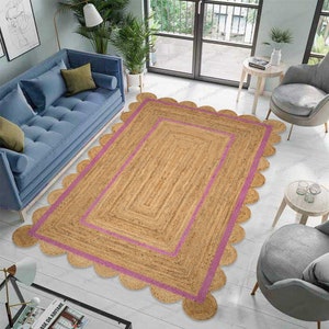 May include: A natural fiber rug with a scalloped edge and a pink border. The rug is made of jute and has a natural, earthy look.