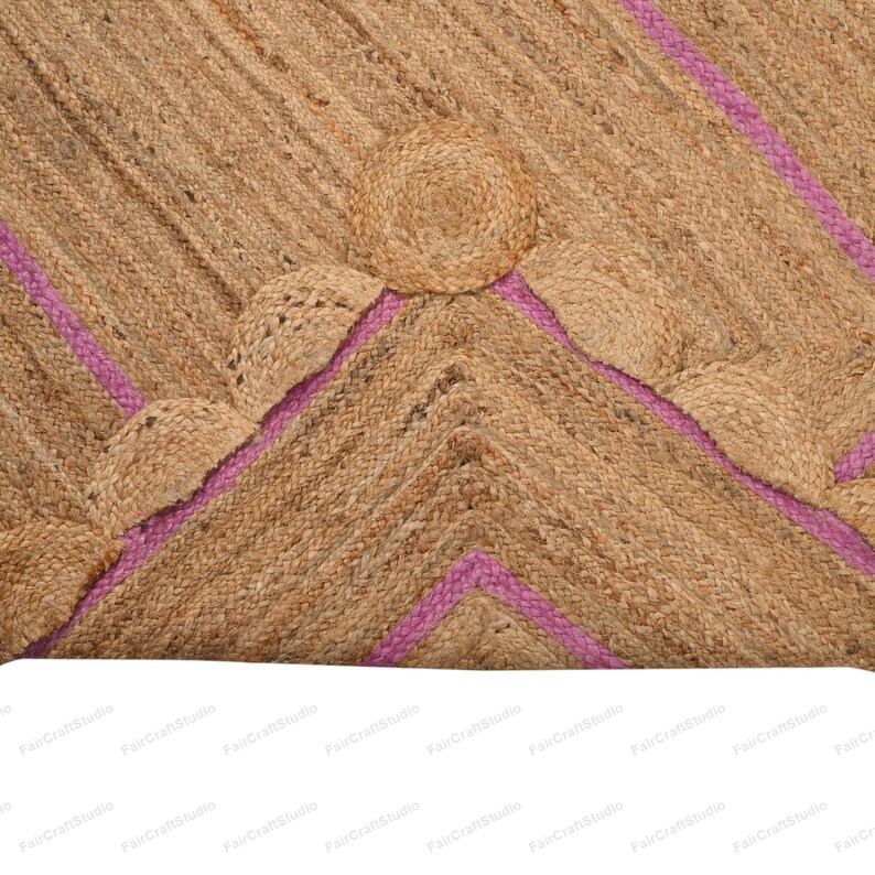 May include: A natural fiber rug with a geometric pattern of pink stripes and woven circles. The rug is made of jute and has a natural, earthy color.