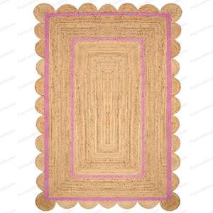 May include: A natural fiber rug with a pink border and scalloped edges. The rug has a woven texture and a rectangular shape.