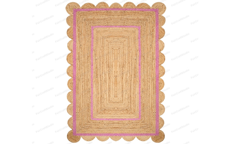 May include: A natural fiber rug with a pink border and scalloped edges. The rug has a woven texture and a rectangular shape.