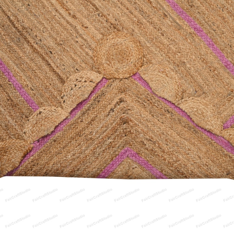 May include: A natural fiber rug with a geometric pattern of pink stripes and woven circles. The rug is made of jute and has a natural, earthy color.