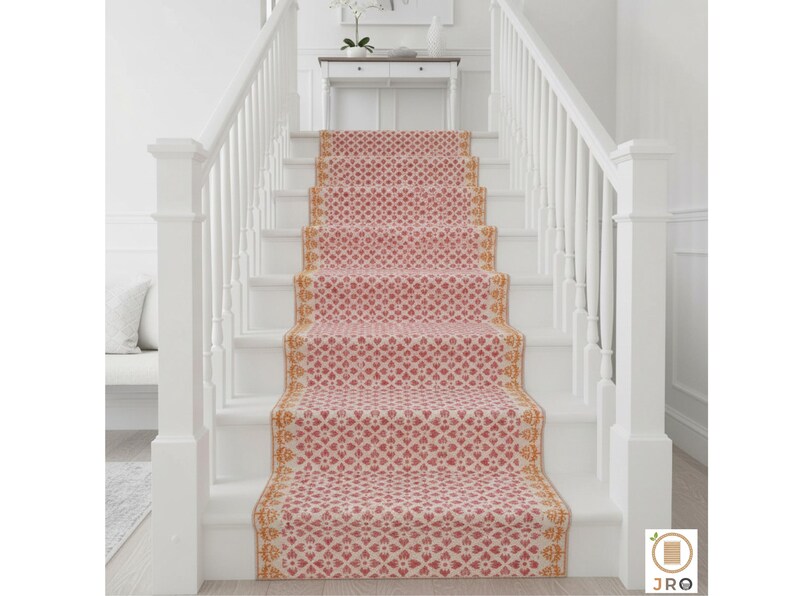 May include: A stair runner featuring a repeating heart pattern in red and cream. The runner is edged with a gold and cream design. The stairs are white with white banisters. The runner adds a decorative touch to the staircase.