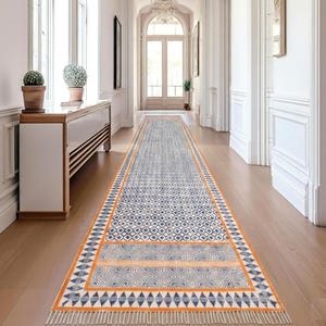 Puede incluir: Una alfombra larga y rectangular con un patrón geométrico en azul, blanco y naranja. La alfombra tiene flecos en los extremos y está colocada sobre un suelo de madera en un pasillo. El diseño incluye patrones de diamantes, triángulos y espirales.