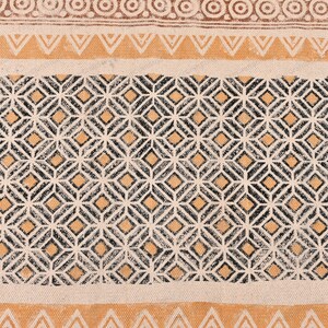 May include: A beige fabric with a black and orange geometric pattern. The pattern is made up of repeating diamonds and squares.