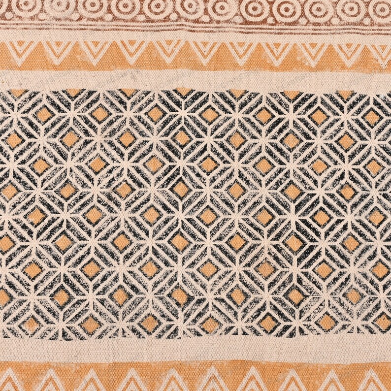 May include: A beige fabric with a black and orange geometric pattern. The pattern is made up of repeating diamonds and squares.