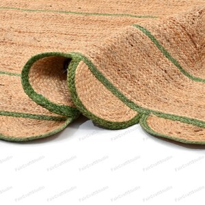 May include: A close-up of a natural fiber rug with green trim. The rug is made of jute and has a woven texture. The rug is folded in half, showing the green trim on both sides.