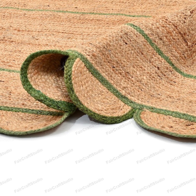 May include: A close-up of a natural fiber rug with green trim. The rug is made of jute and has a woven texture. The rug is folded in half, showing the green trim on both sides.