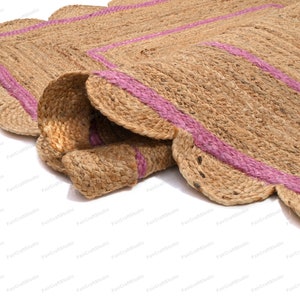 May include: A natural fiber rug with a scalloped edge and pink stripes. The rug is made of jute and is a natural color.