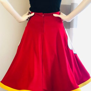 Red high-waisted A-line skirt with yellow trimmed hem, featuring hidden pocket Mickey glove fabric appliqués. Two white vinyl ovals at the center front represent Mickey Mouse's pants.