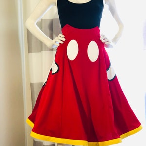 Red high-waisted A-line skirt with yellow trimmed hem, featuring hidden pocket Mickey glove fabric appliqués. Two white vinyl ovals at the center front represent Mickey Mouse's pants.