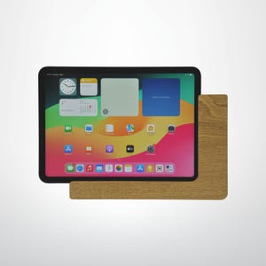 Puede incluir: Una tableta negra que muestra una pantalla de inicio colorida, apoyada en un soporte de madera marrón claro. La pantalla muestra iconos de aplicaciones y un reloj. El soporte es rectangular y de madera.