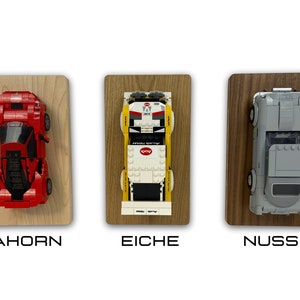 May include: Three Lego car models displayed on wooden plaques. The cars are a red Ferrari, a yellow and white Audi, and a gray Porsche. The plaques are labeled "Ahorn", "Eiche", and "Nuss".