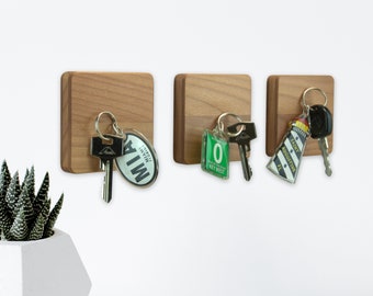 May include: Three wooden key holders with metal key hooks and keychains. The keychains have different designs, including a green and white Key West keychain, a green and white lighthouse keychain, and a green and white MIA keychain.