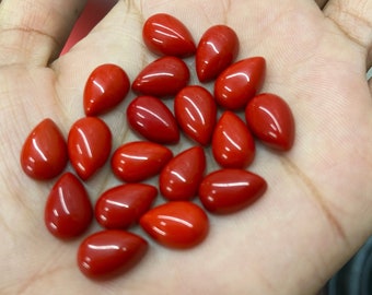 May include: A collection of 18 red teardrop-shaped gemstones. The gemstones are smooth and polished, and they are arranged in a loose pile on a person's hand.