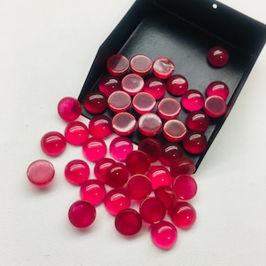 May include: A collection of round, cabochon-cut, pink gemstones in a black tray. The gemstones are smooth and polished, with a slight shine.