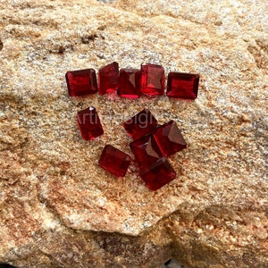 May include: A group of red, square-shaped glass gems on a rough, brown rock surface.