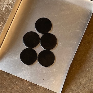 May include: Six black round coasters arranged in a triangular pattern on a silver tray.