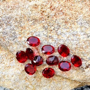 May include: Ten oval-shaped, red gemstones on a rough, brown, textured surface.