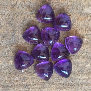 Puede incluir: Diez cabujones de amatista de forma triangular púrpura sobre una superficie de madera.
