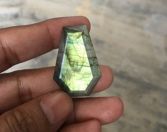 May include: A green and gold labradorite gemstone with a faceted, teardrop shape.