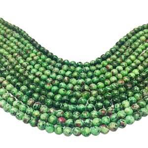 Puede incluir: Una hebra de cuentas de piedras preciosas verdes y rojas. Las cuentas son redondas y tienen un aspecto moteado.