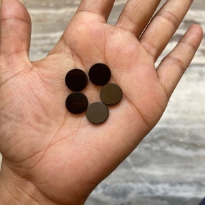 May include: Five black round magnetic discs in a hand. The discs are about 1 inch in diameter.