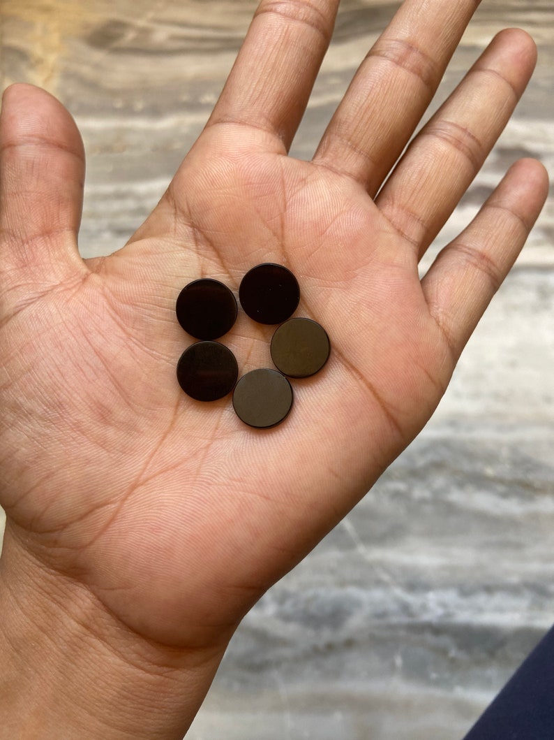 May include: Five black round magnetic discs in a hand. The discs are about 1 inch in diameter.