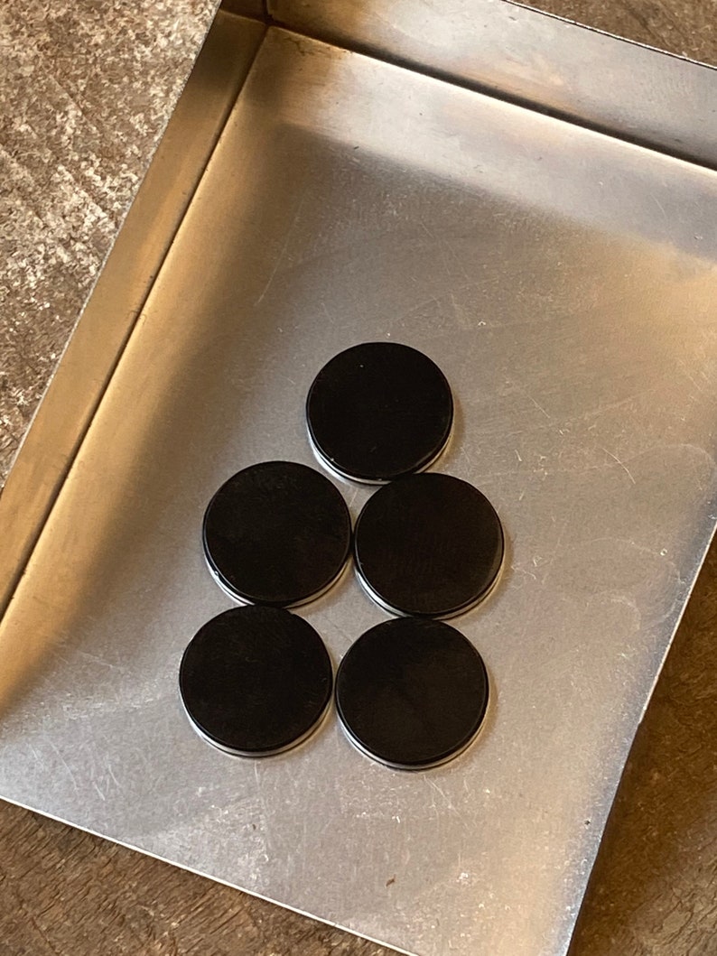 May include: A set of six black round magnetic discs arranged in a pyramid shape on a silver metal surface.