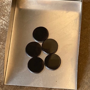 May include: Five black round disc magnets on a silver metal surface.