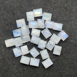 Könnte beinhalten: Eine Sammlung von 18 regenbogenfarbenen weißen Mondstein-Cabochons, die jeweils in quadratischer Form geschnitten sind. Die Steine haben einen dezenten Schimmer und eine milchig weiße Farbe.