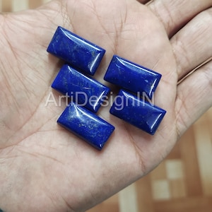 May include: Five rectangular lapis lazuli gemstones, each with a deep blue color and flecks of gold pyrite. The stones are arranged on a hand.