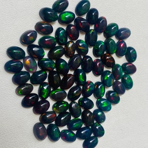Puede incluir: Un conjunto de &oacute;palos negros de forma ovalada con vibrantes destellos de color, incluyendo verde, rojo y dorado. Las piedras preciosas est&aacute;n dispuestas juntas, mostrando sus superficies pulidas y su juego de colores iridiscente. Ideales para joyer&iacute;a.