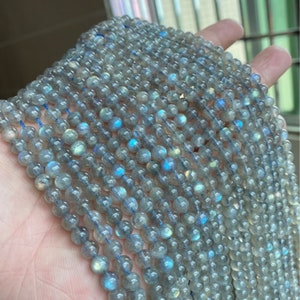 Può includere: Una collana di perle rotonde in labradorite grigia con riflessi iridescenti blu e verdi. Le perle sono infilate su un filo sottile blu.