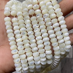 May include: A strand of white iridescent shell beads. The beads are round and have a smooth, polished finish. They are strung on a white thread.