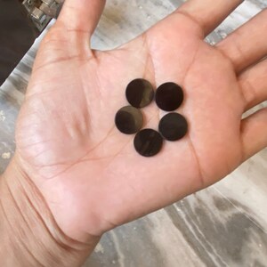 May include: Five black round buttons, possibly for a craft project or clothing, are displayed on the palm of a hand.